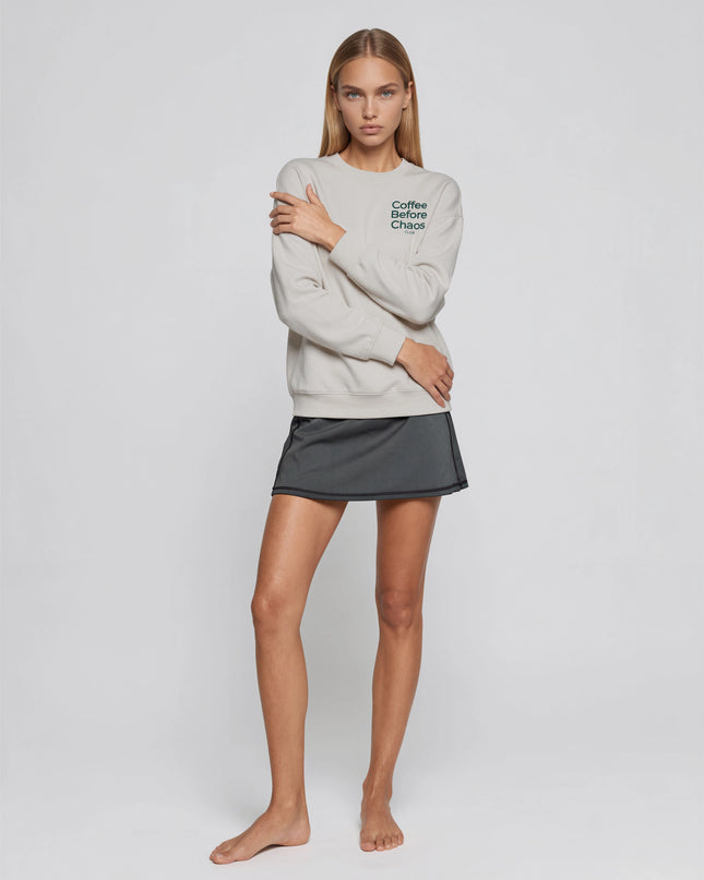 Model wearing the Tuvi Coffee Before Chaos Crewneck in gray, seen from the front, showing the small dark green chest print and the relaxed mid-weight fit.